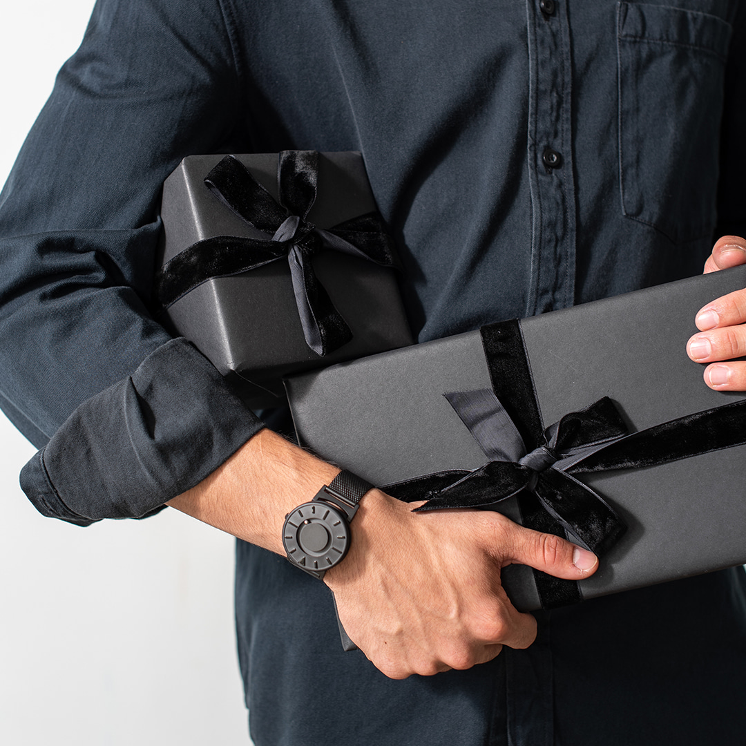 검은 리본으로 포장된 선물 박스를 들고있는 남자의 손