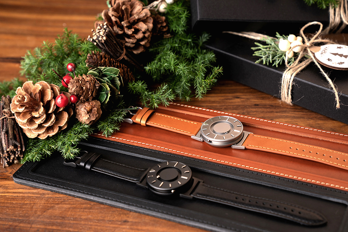 블랙, 브라운 시계 트레이 위에 각각 놓여있는 브래들리 x 디진, 브래들리 보이저 제품. 주변에는 크리스마스 분위기가 나는 소품들로 장식되어 있어요.