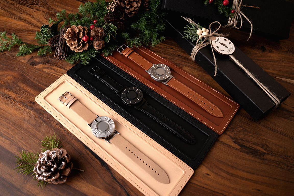 베이지, 블랙, 브라운 시계 트레이 위에 각각 놓여 있는 브래들리 엣지 실버, 브래들리 x 디진, 브래들리 보이저 제품. 주변에는 크리스마스 분위기가 나는 소품들로 장식되어 있어요.